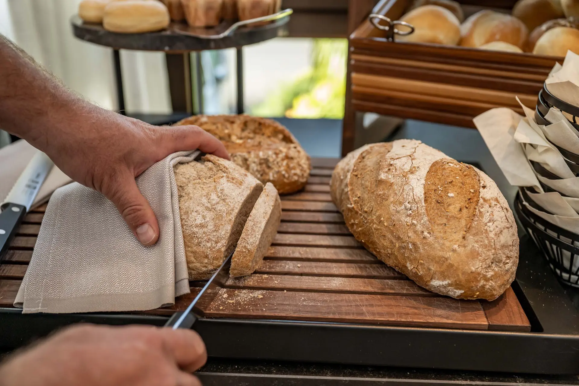 Eindrücke aus dem La Val Hotel & Spa Hand schneidet ein frisch gebackenes Brot auf einem Holzbrett