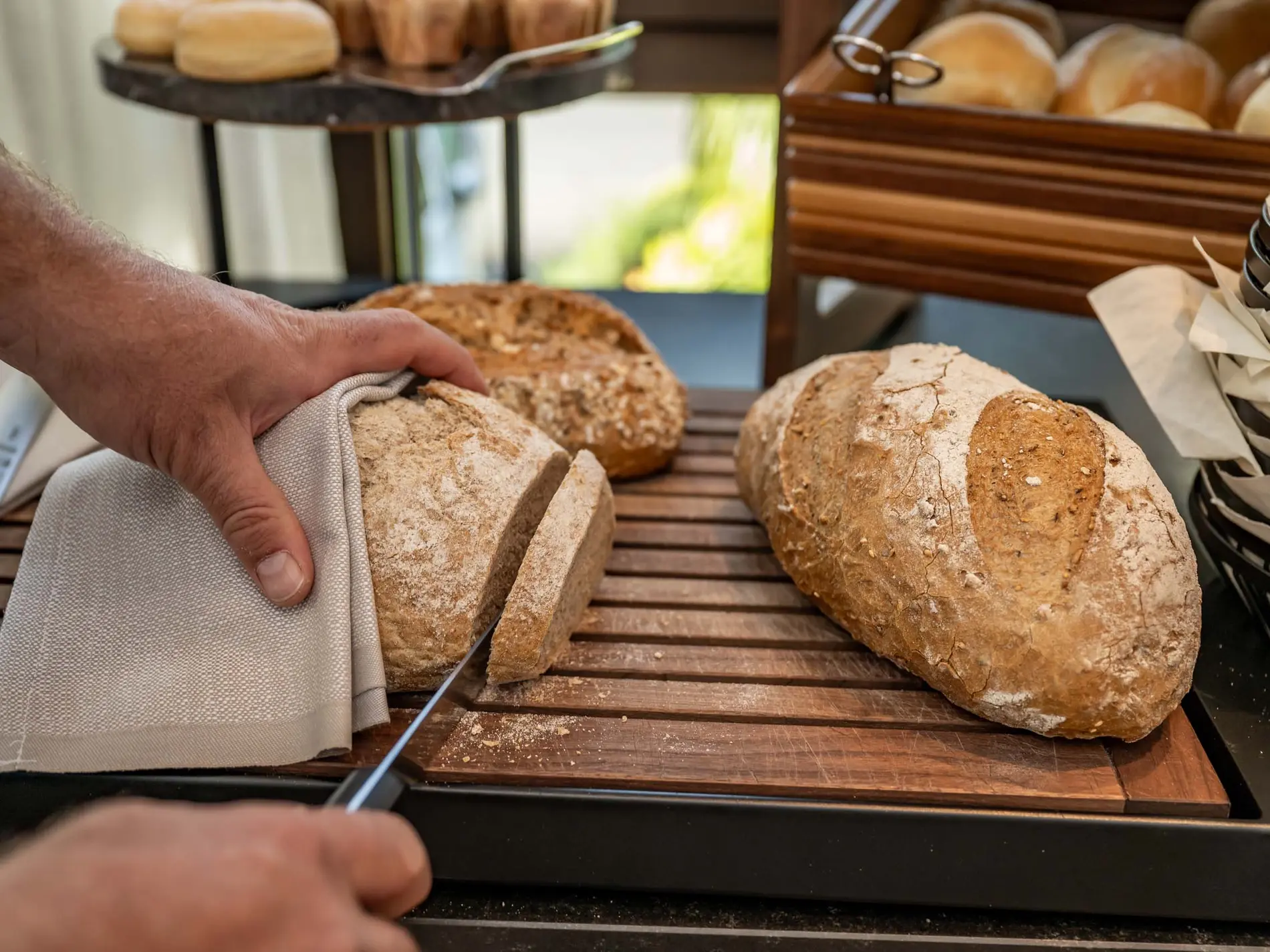 Kulinarische Vielfalt in unseren Restaurants in Brigels Hand schneidet ein frisch gebackenes Brot auf einem Holzbrett
