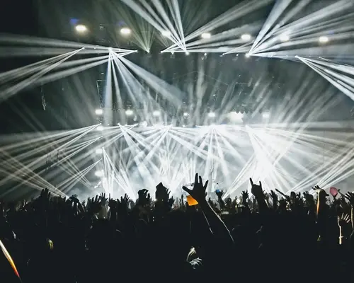 Menschenmenge bei einem Konzert mit hellen Bühnenlichtern und erhobenen Händen