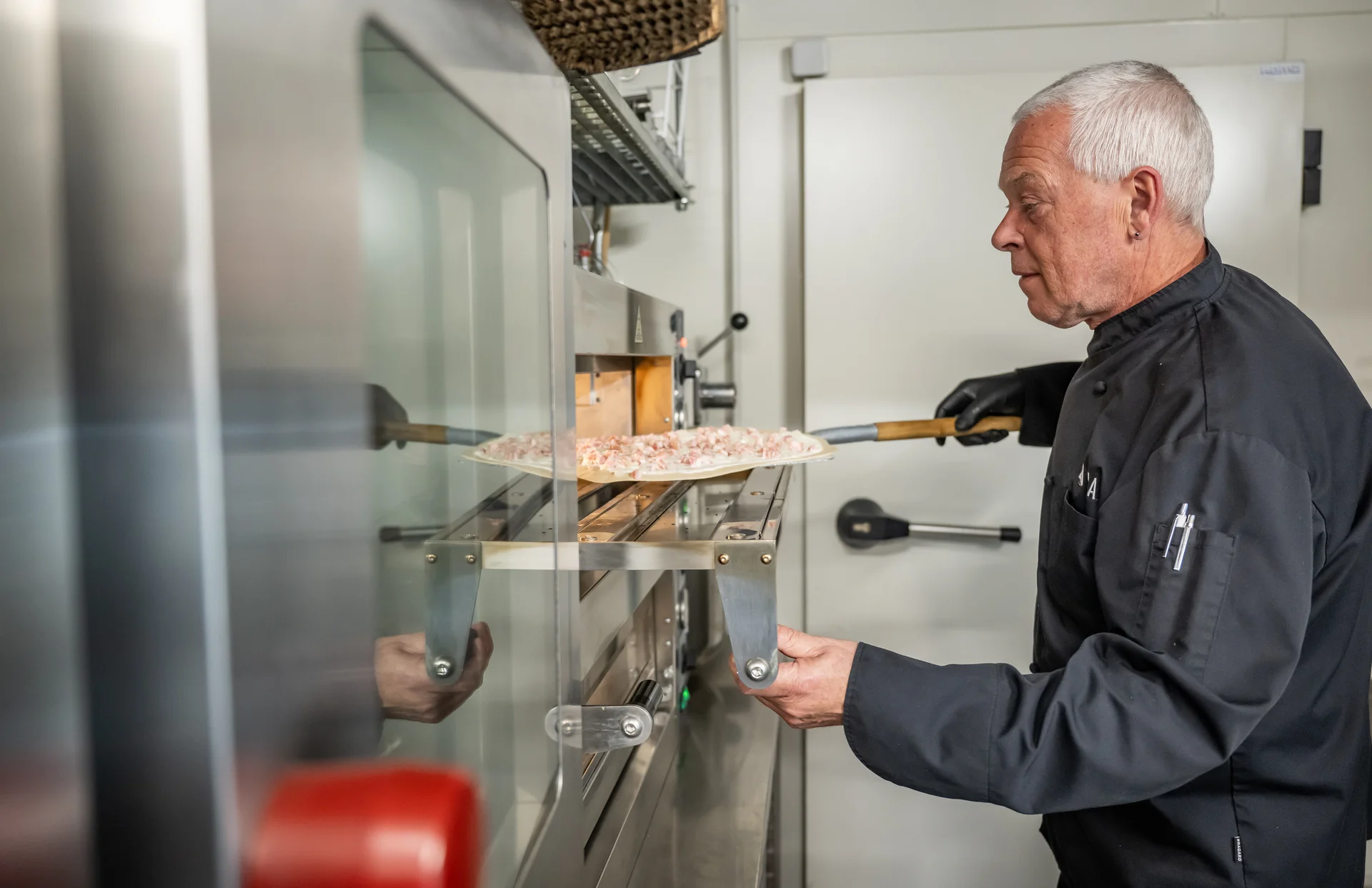 Älterer Bäcker schiebt Pizza in gewerbliche Ofenanlage