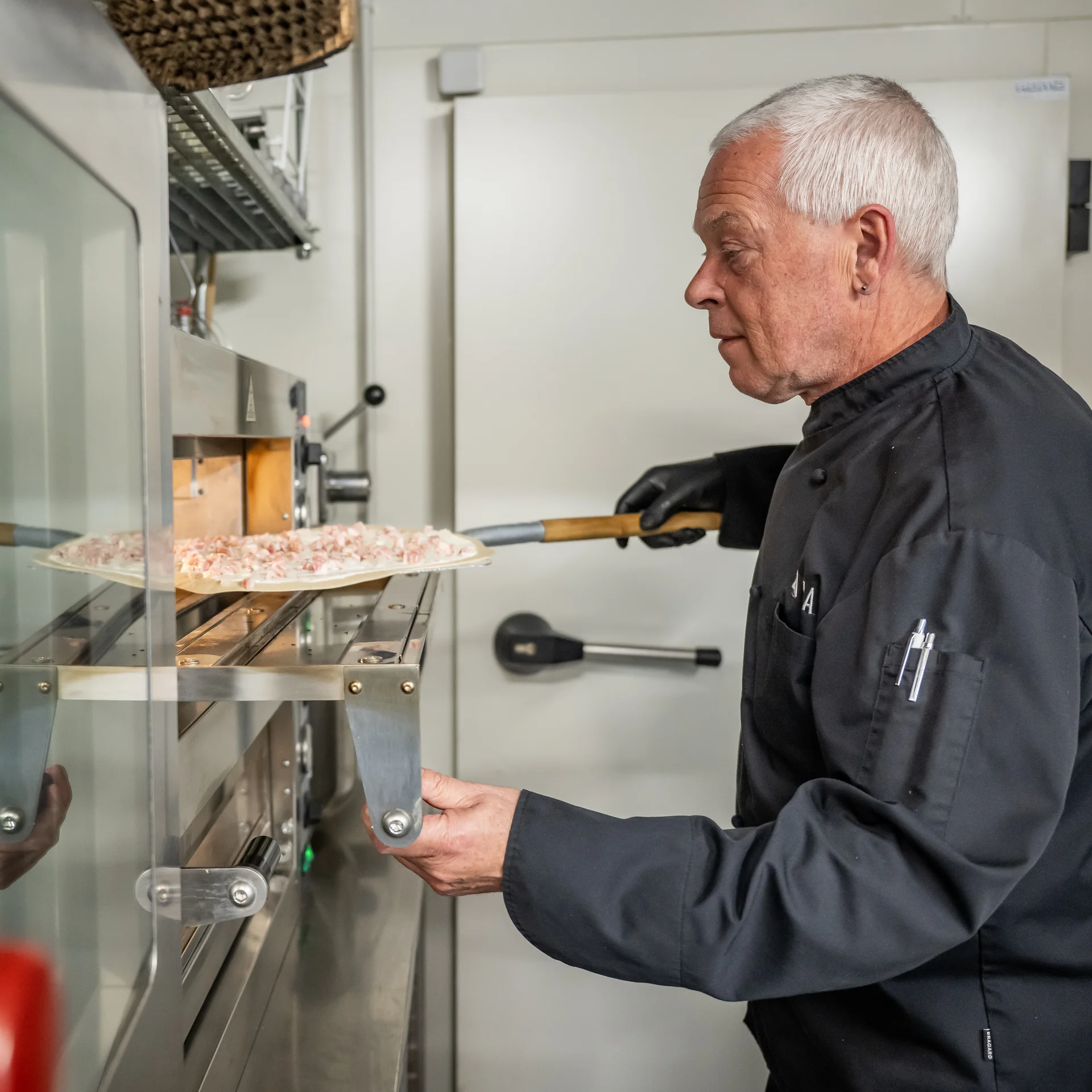Älterer Bäcker schiebt Pizza in gewerbliche Ofenanlage