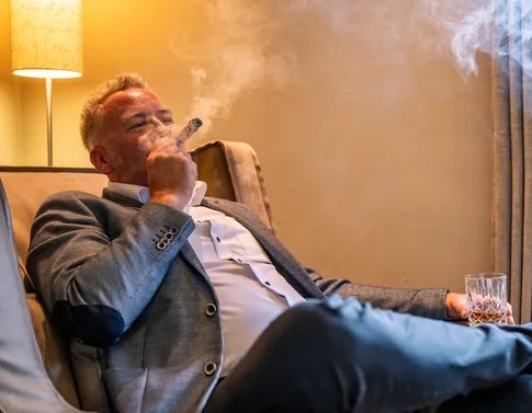 Mann im Anzug raucht Zigarre und hält ein Glas Whisky