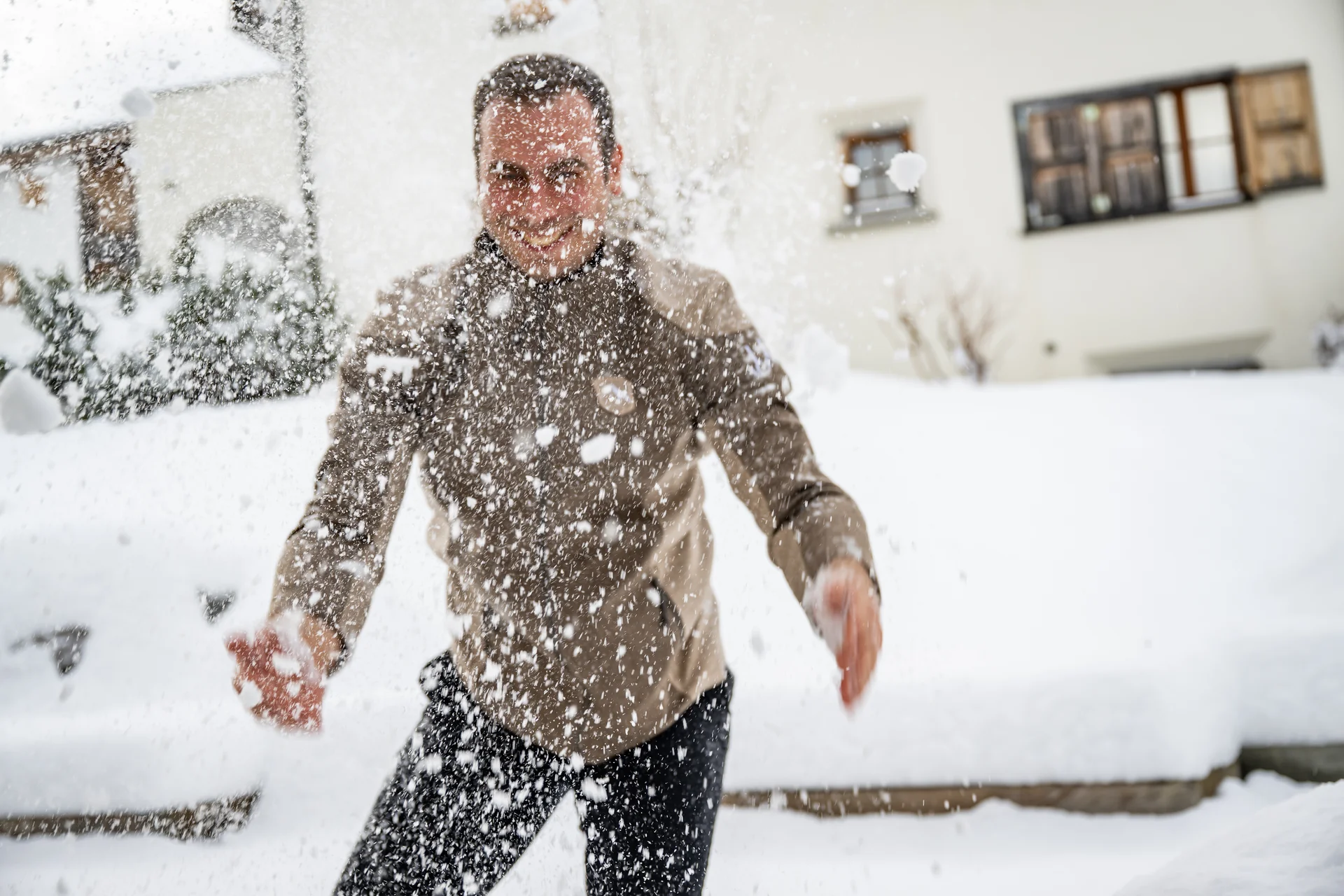 Mann wirft Schnee im Garten eines schneebedeckten Hauses