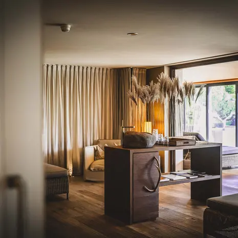 La Val Hotel & Spa: Ihr Hotel in Breil/Brigels Gemütlicher Raum mit Vorhängen, Sessel, Holzregal und getrockneten Pflanzen