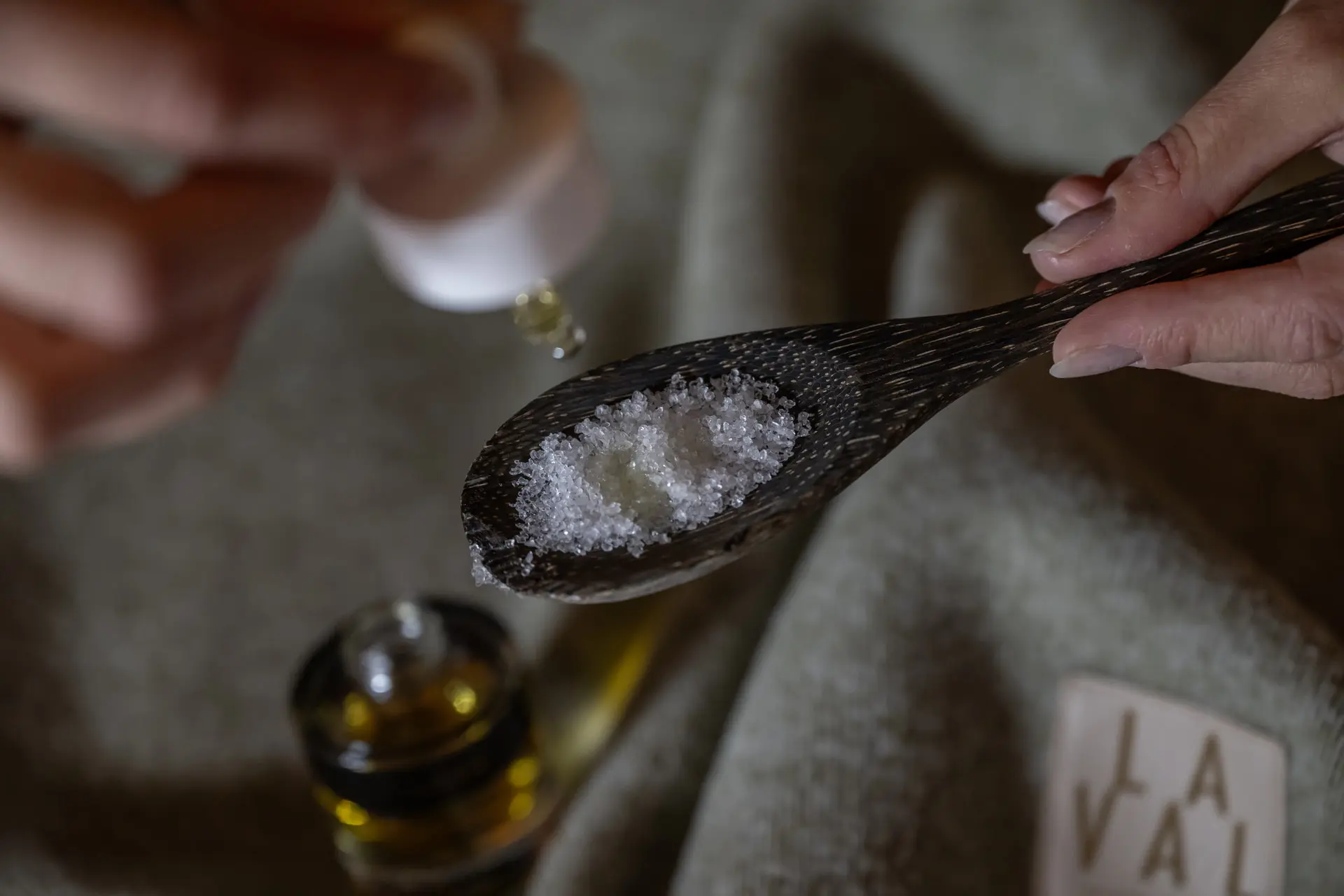 Eindrücke aus dem La Val Hotel & Spa Hand gibt Tropfen Öl auf grobes Salz in einem Holzlöffel