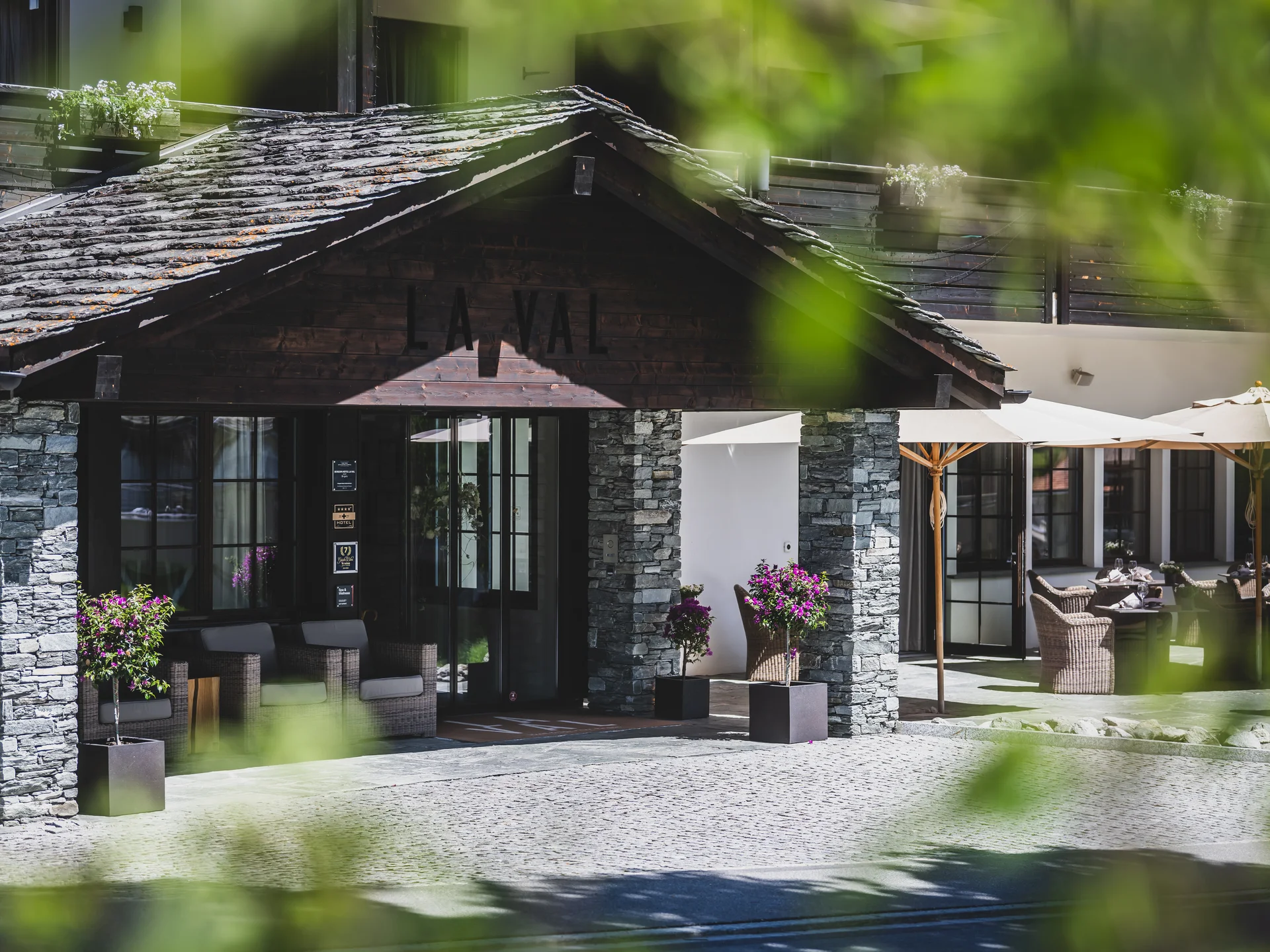 Eingang eines Hotels mit Steinpfeilern und Terrasse mit Sonnenschirmen