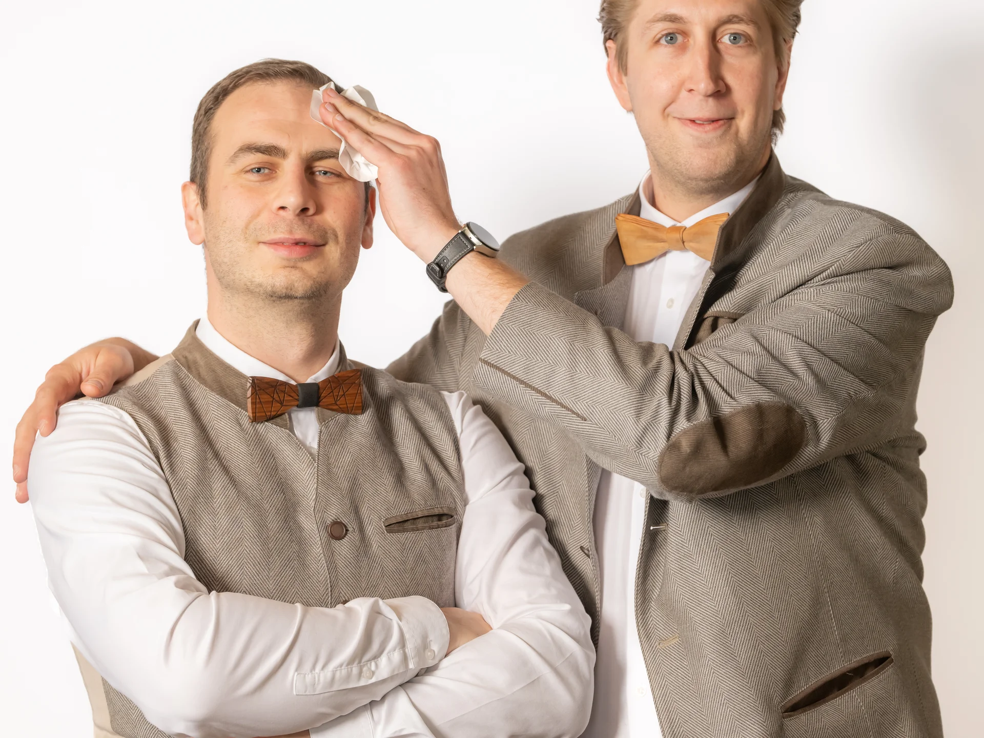 Zwei Männer in traditionellen Anzügen, einer wischt Stirn des anderen ab