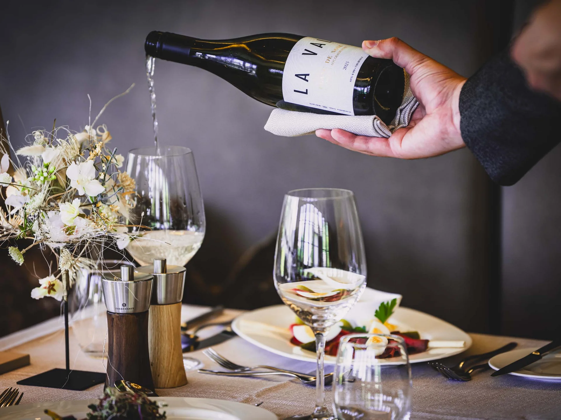 Wein wird in ein Glas auf einem elegant gedeckten Tisch mit Blumen und Besteck eingeschenkt