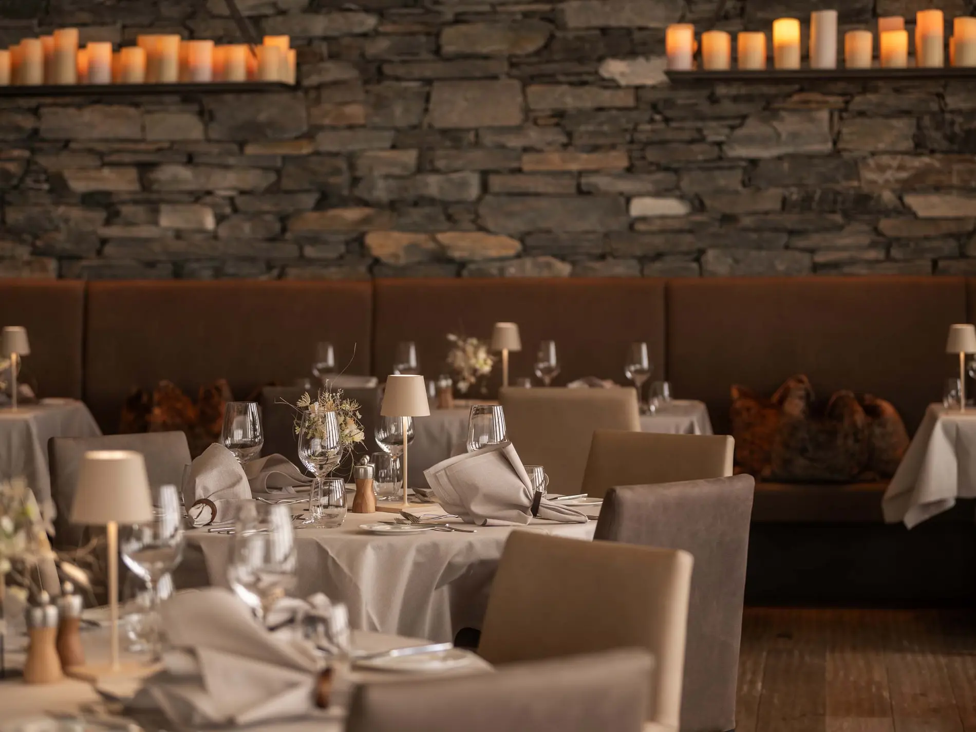 Kulinarische Vielfalt in unseren Restaurants in Brigels Elegantes Restaurant mit gedeckten Tischen, Kerzen und Steinwand