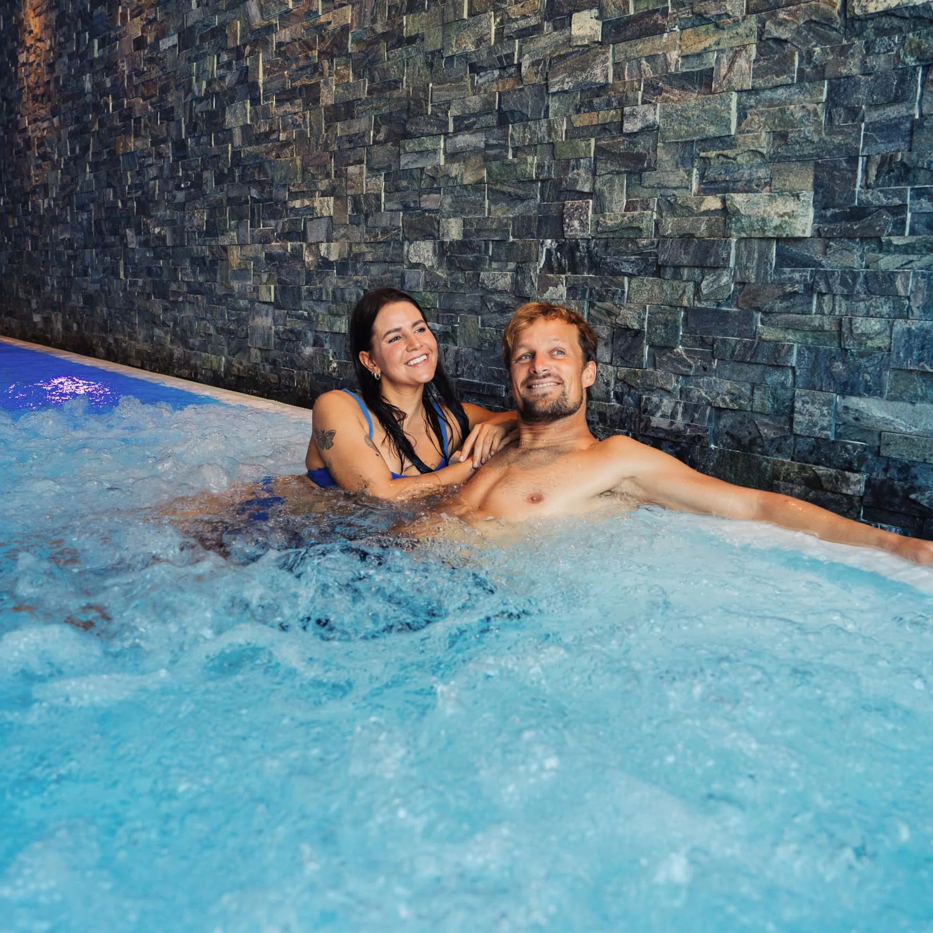 Paar entspannt im Innenwhirlpool mit steinerner Wand im Hintergrund