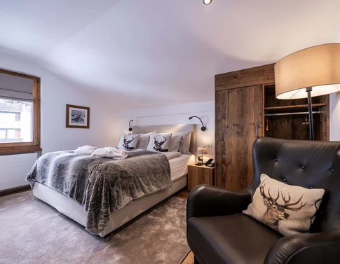 Gemütliches Schlafzimmer mit Bett, Fell-Decke, Lederstuhl und Holzkleiderschrank