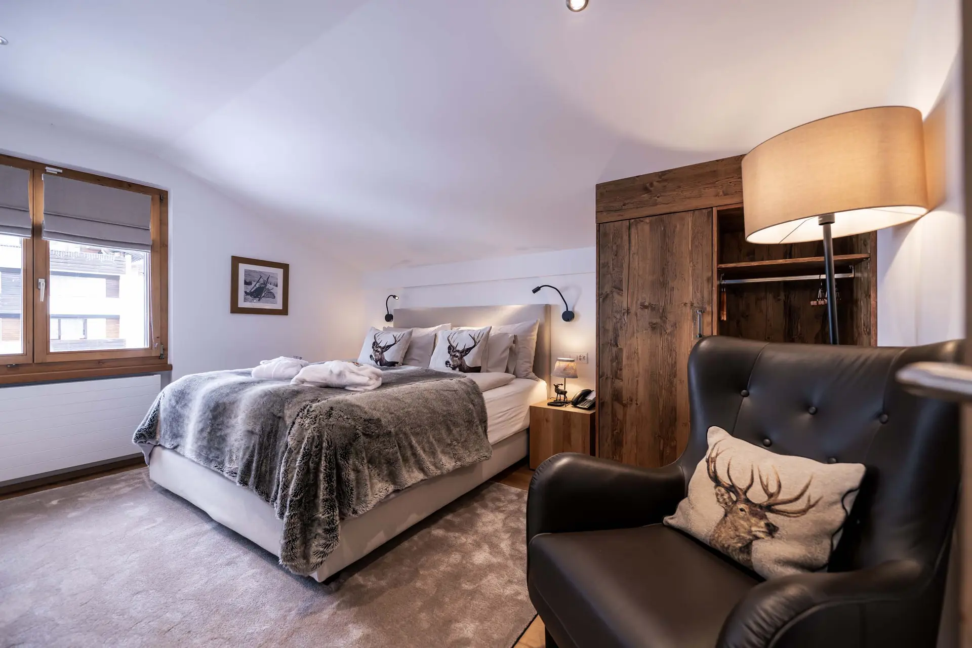 Eindrücke aus dem La Val Hotel & Spa Gemütliches Schlafzimmer mit Bett, Fell-Decke, Lederstuhl und Holzkleiderschrank