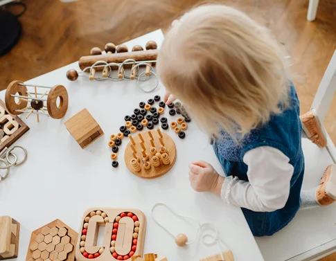 Kleines Kind spielt mit verschiedenen hölzernen Lernspielzeugen auf einem weißen Tisch