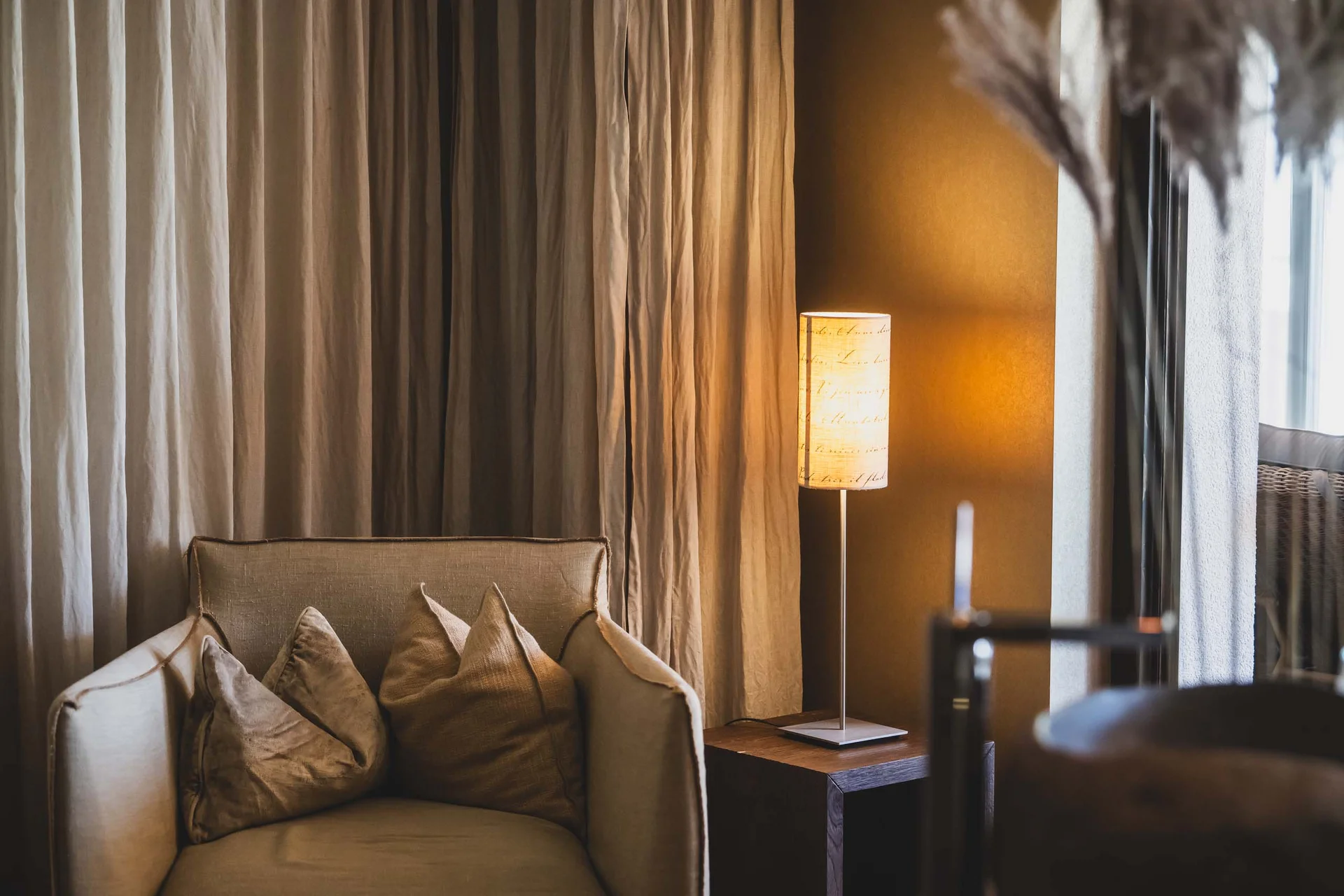 Gemütlicher beiger Sessel mit Kissen neben einer beleuchteten Stehlampe bei Vorhängen