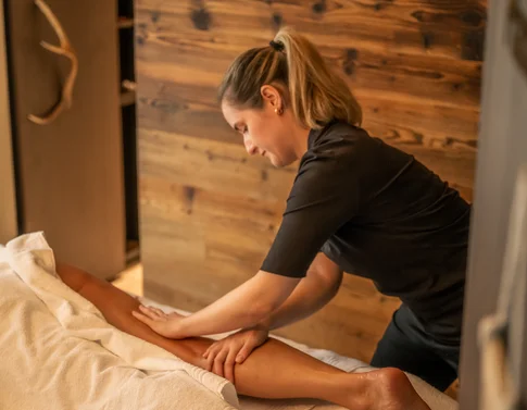 Frau massiert Bein einer Person in einem Wellnessraum mit Holzwänden