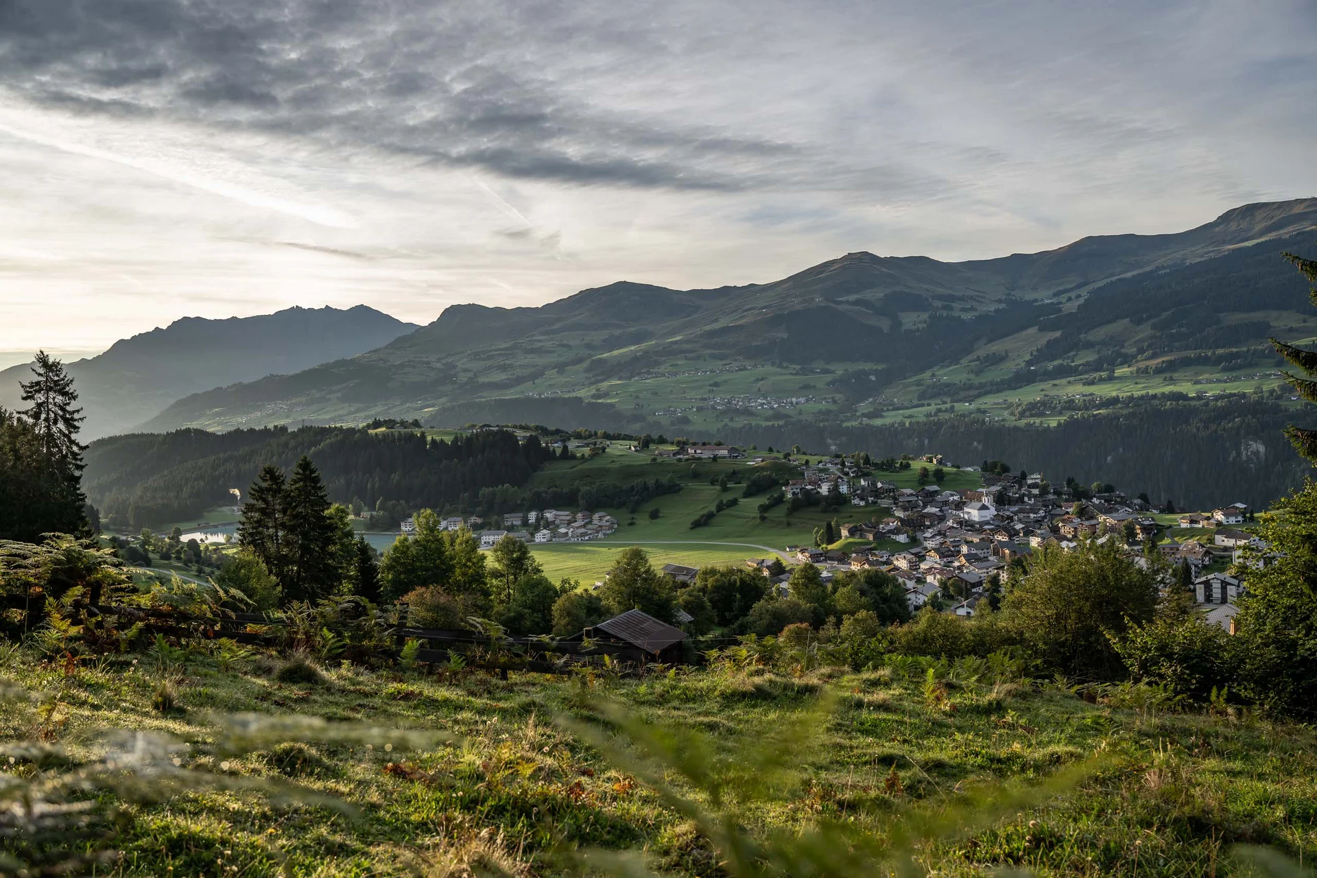 Dorf und grüne Hügel vor bewölkten Bergen in der Abenddämmerung