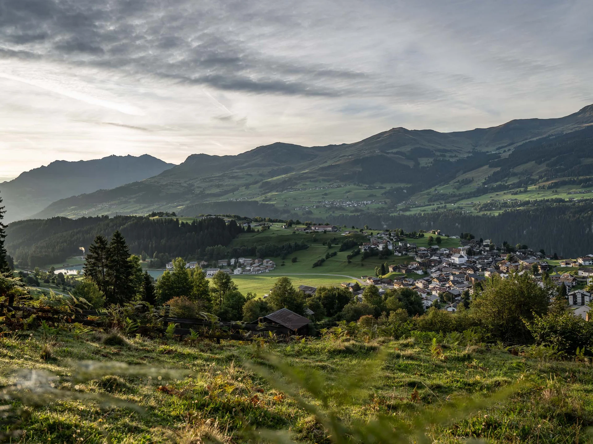 Dorf und grüne Hügel vor bewölkten Bergen in der Abenddämmerung