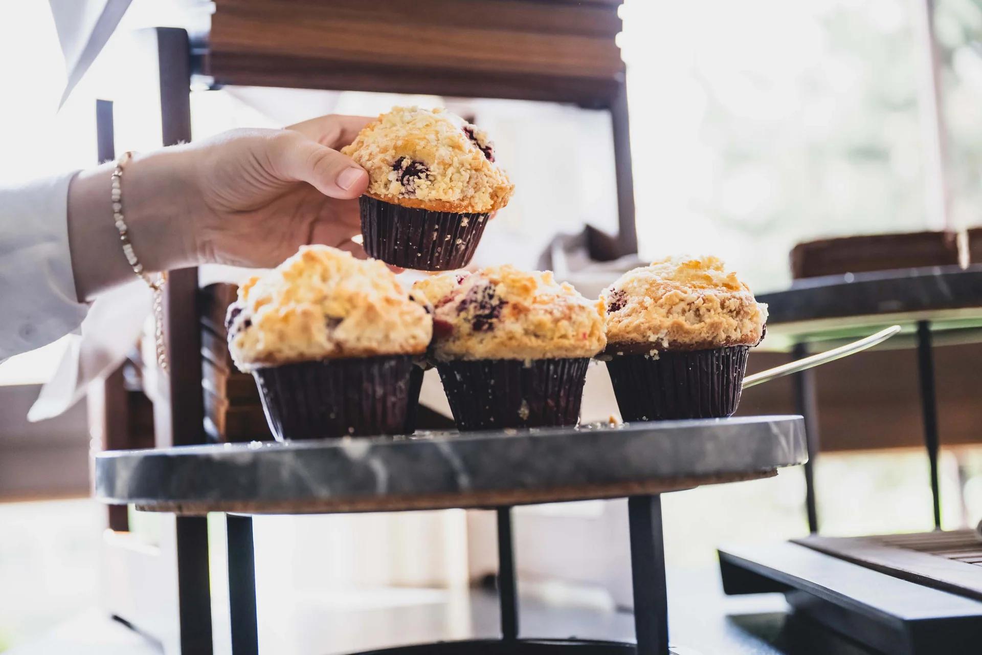 Hand nimmt einen Muffin von einem Tisch mit mehreren Muffins