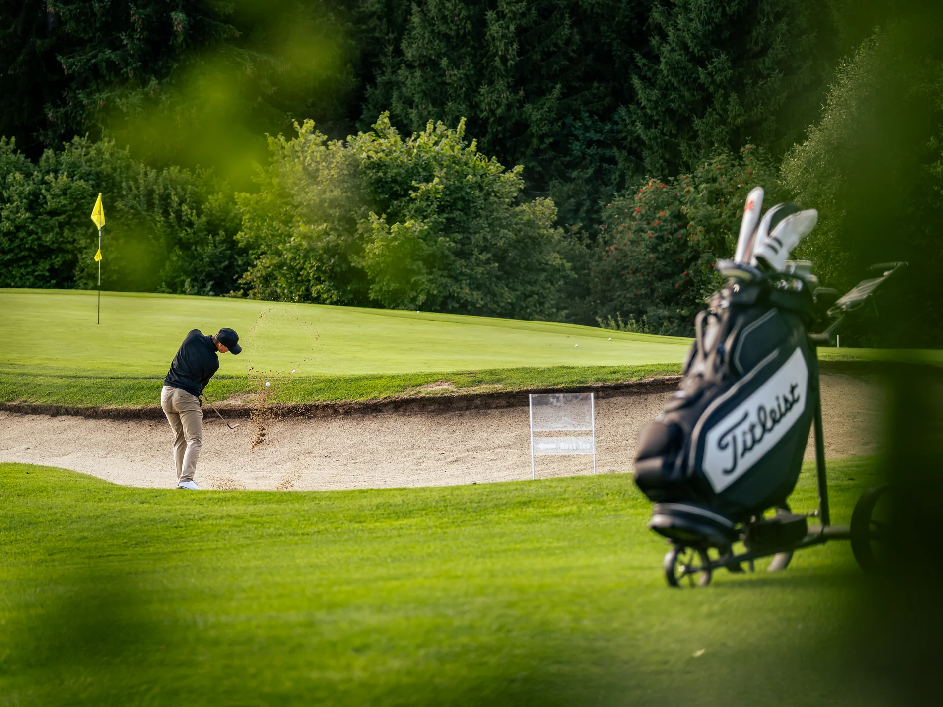 Golfer schlägt Ball aus dem Sandbunker auf Golfplatz mit Golfbag im Vordergrund