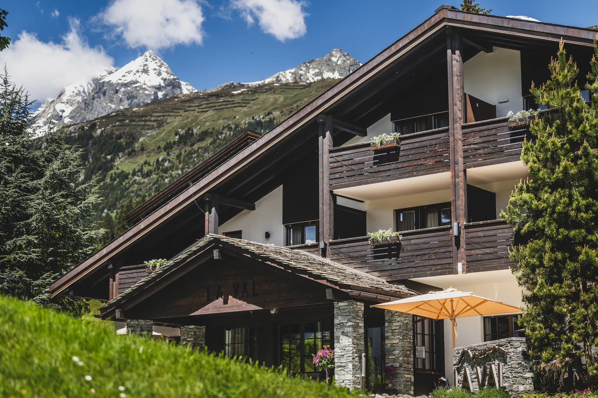 Alpenhotel mit Holzbalkonen vor schneebedeckten Bergen und blauem Himmel