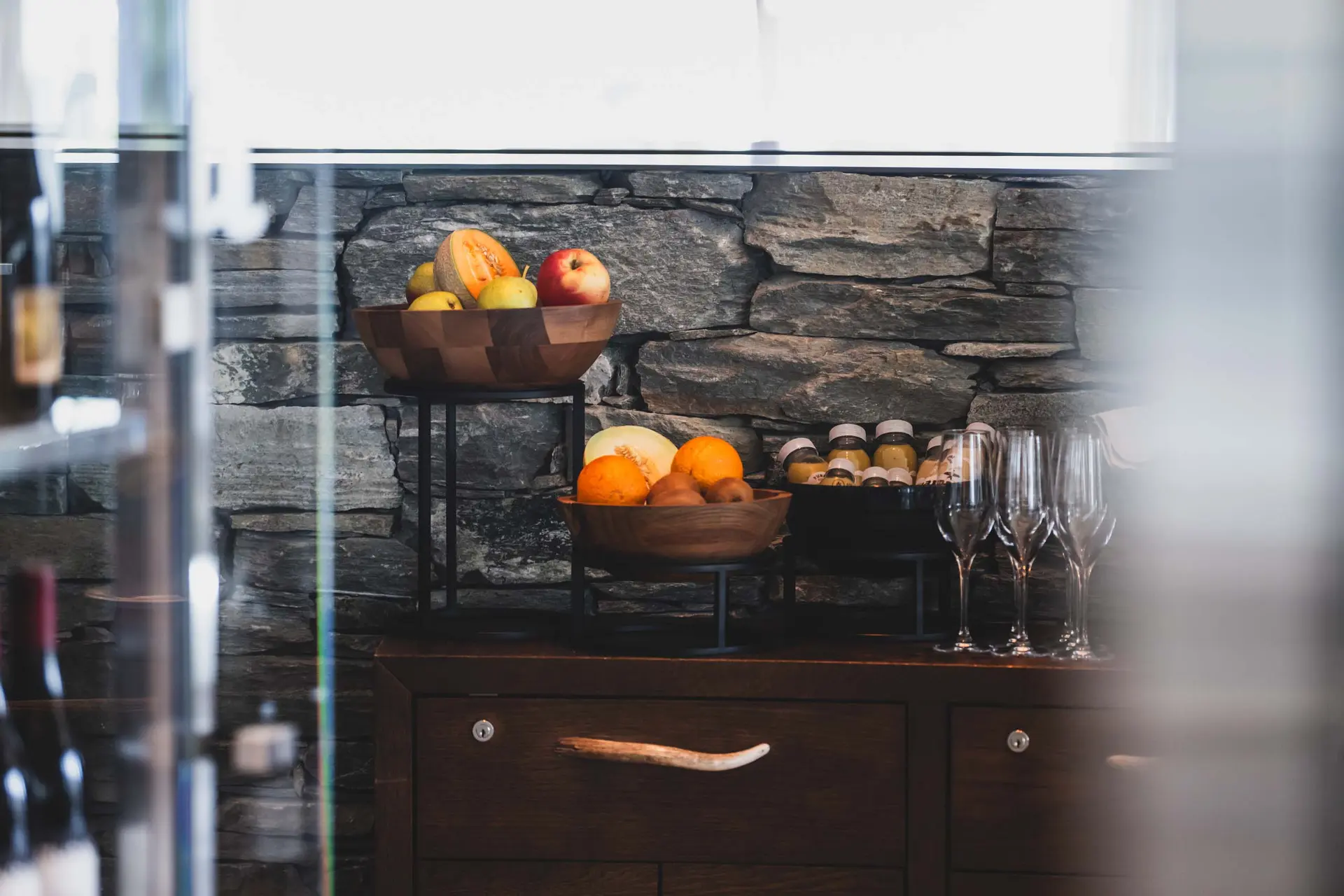 Eindrücke aus dem La Val Hotel & Spa Holzschalen mit Früchten und Flaschen auf einem Holzmöbel vor Steinmauer