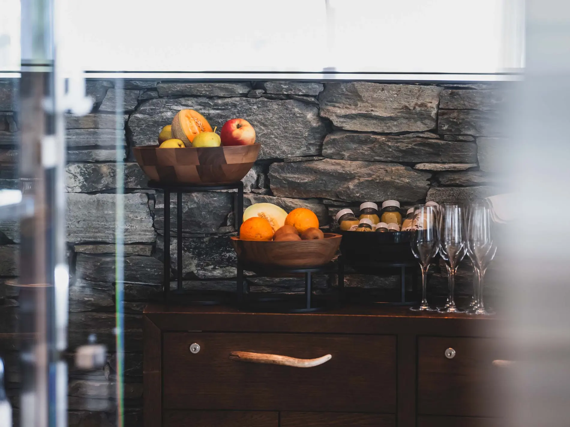 Kulinarische Vielfalt in unseren Restaurants in Brigels Holzschalen mit Früchten und Flaschen auf einem Holzmöbel vor Steinmauer