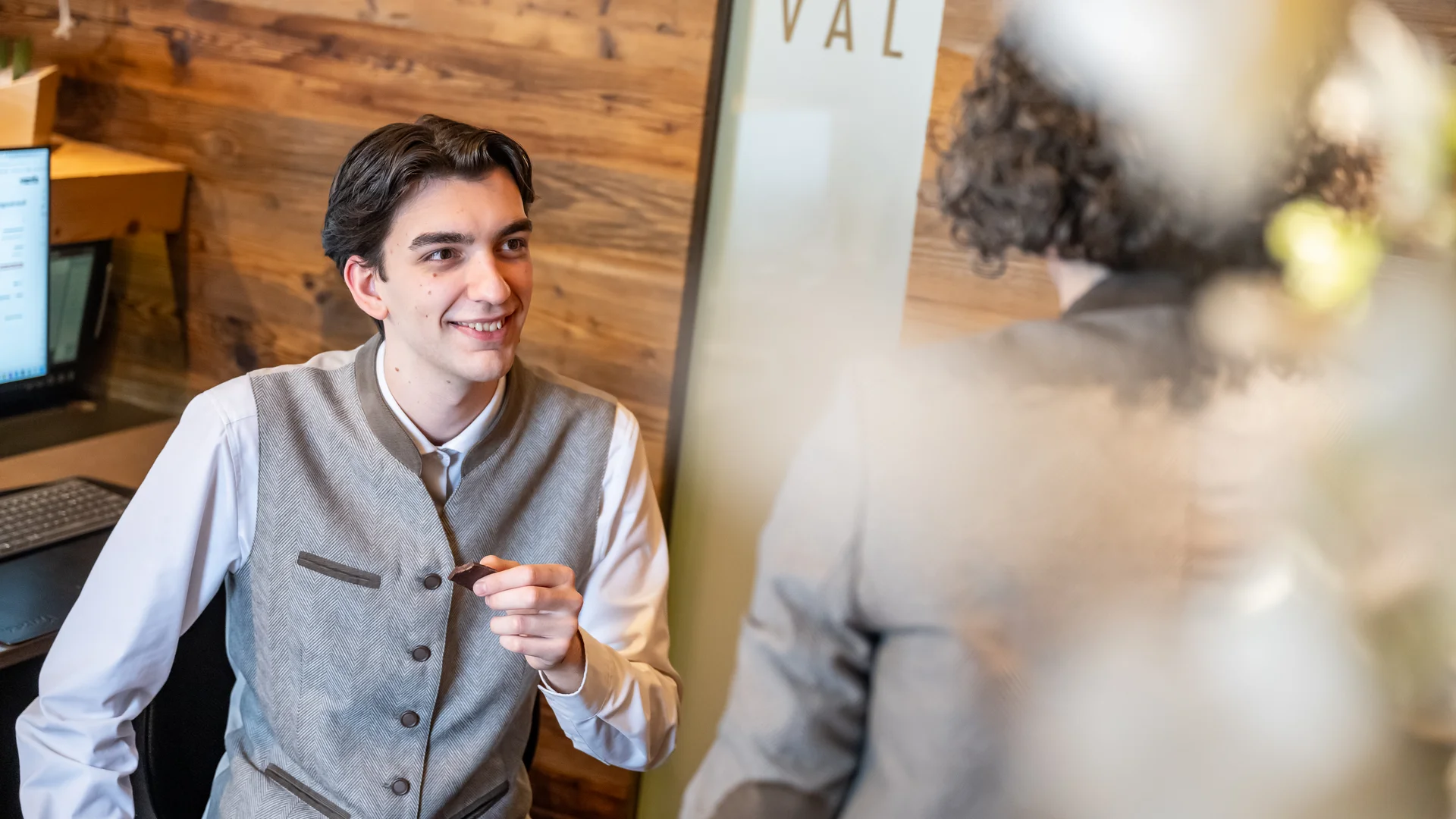 Mann in Trachtenweste lächelt und spricht mit Person in Geschäftsumgebung