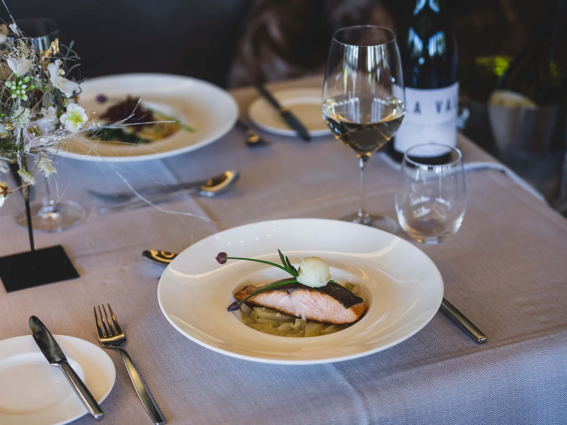 Lachsfilet auf Gemüse angerichtet mit Glas Weißwein auf gedecktem Tisch