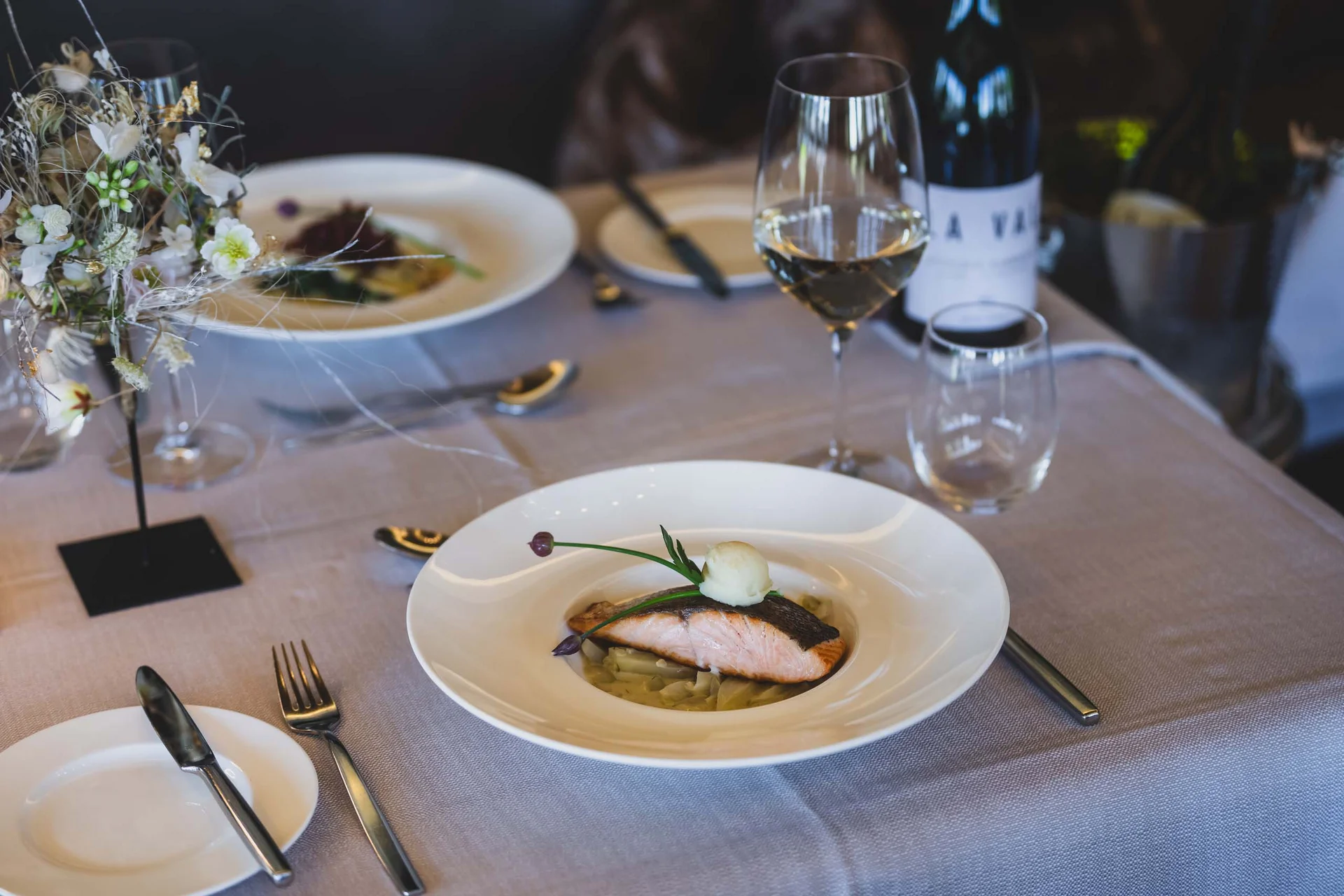 Lachsfilet auf Gemüse angerichtet mit Glas Weißwein auf gedecktem Tisch