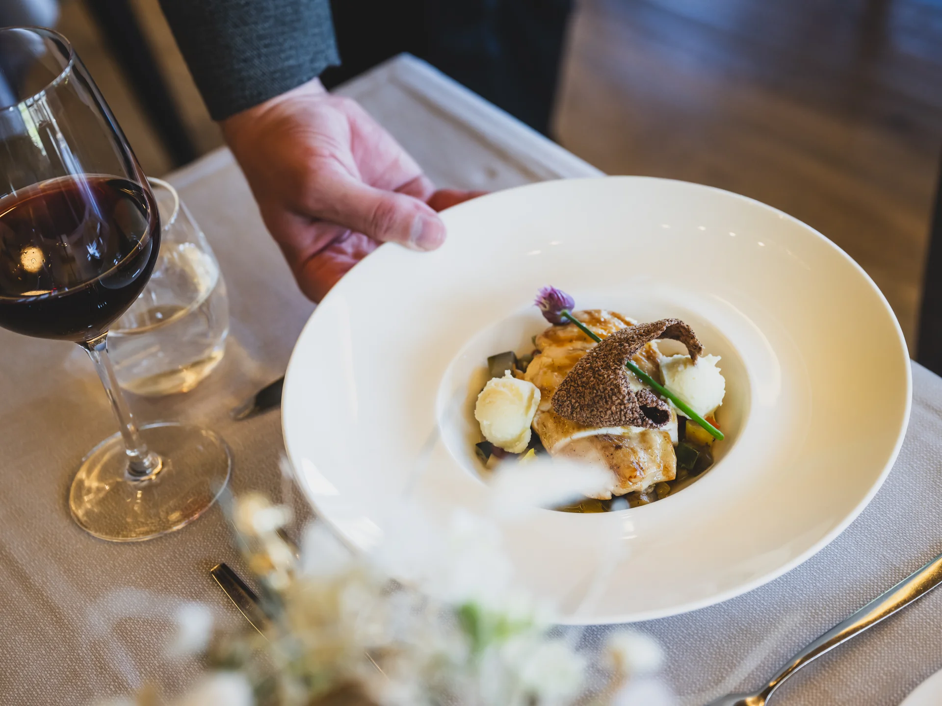 Elegantes serviertes Gericht auf weißem Teller mit Glas Rotwein auf Tisch