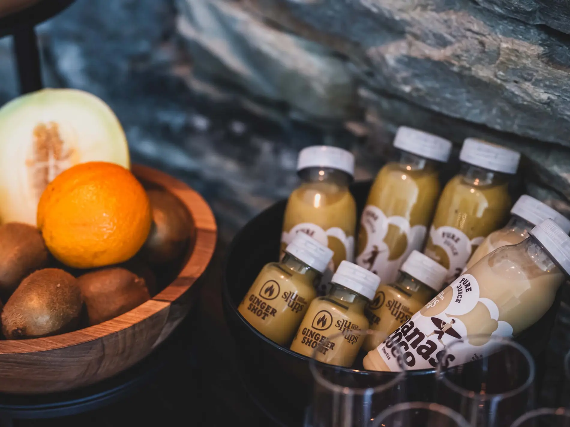 Kulinarische Vielfalt in unseren Restaurants in Brigels Flaschen mit Ingwershots und Bananen-Kokos-Saft neben Schale mit Obst