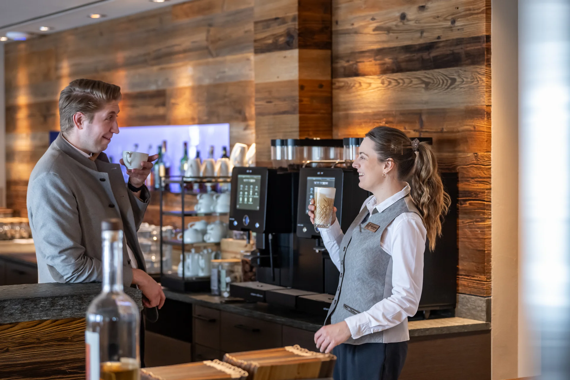 Mann und Frau lachen und trinken Kaffee an einer Kaffeebar mit Holzverkleidung.