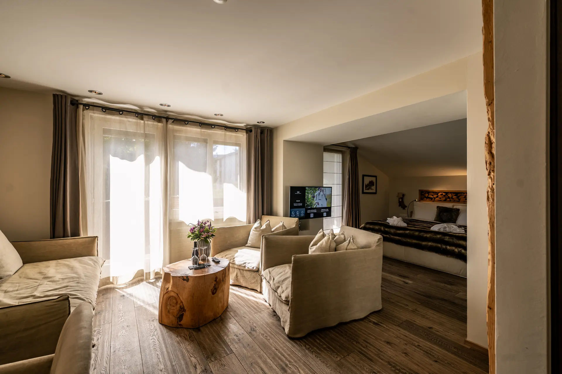 Eindrücke aus dem La Val Hotel & Spa Wohnbereich mit beige Sofas, Holz-Couchtisch und Blick ins Schlafzimmer