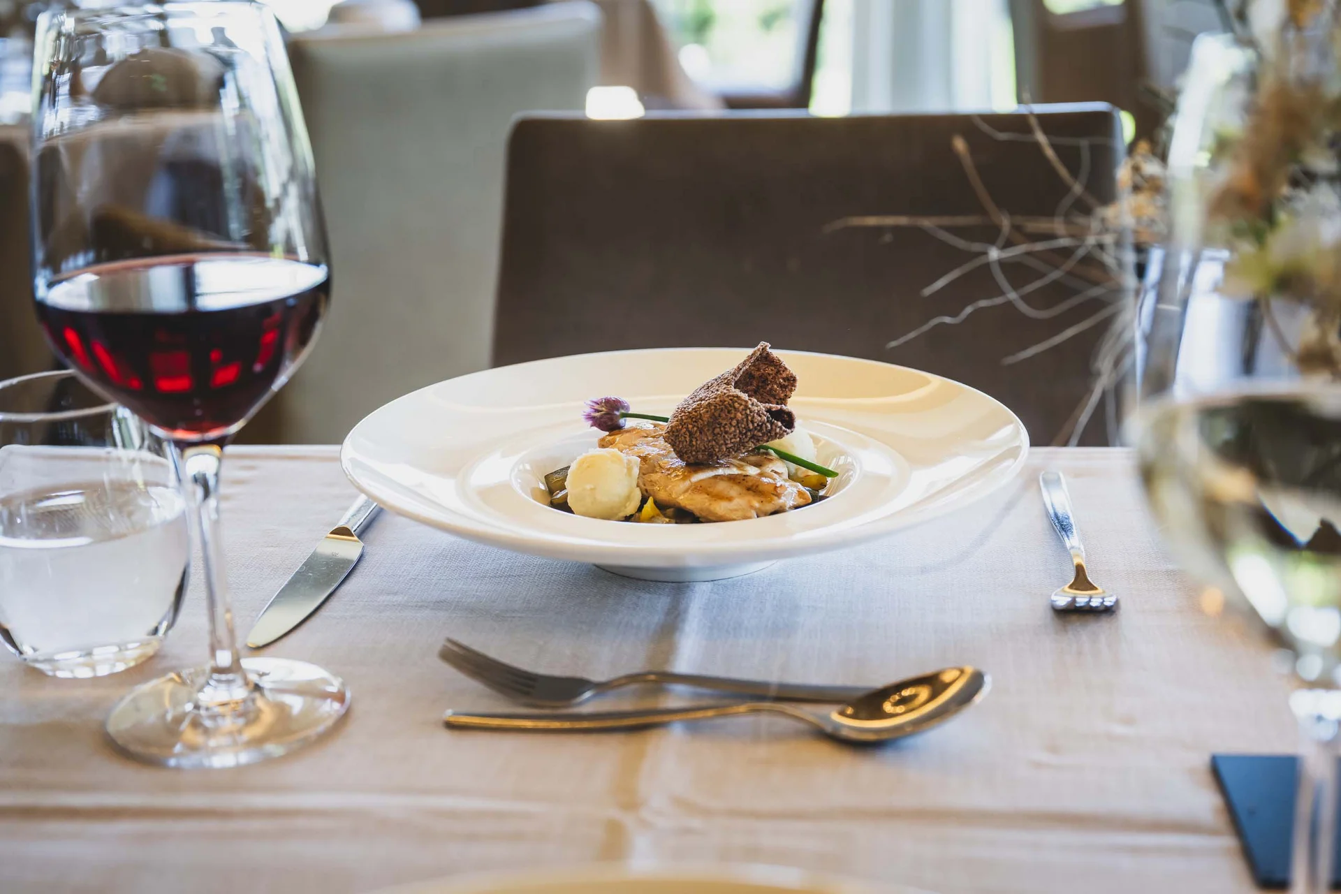 Elegantes Restaurantgericht mit Rotwein und Tischgedeck auf weißer Tischdecke
