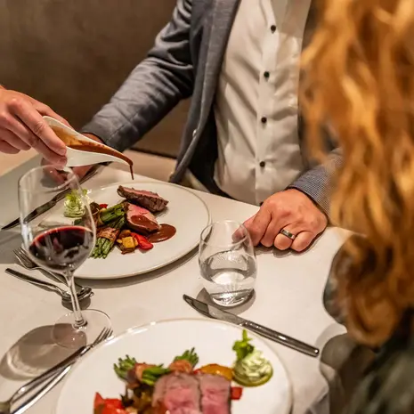 Person pouring sauce over a meat dish in a fine dining restaurant