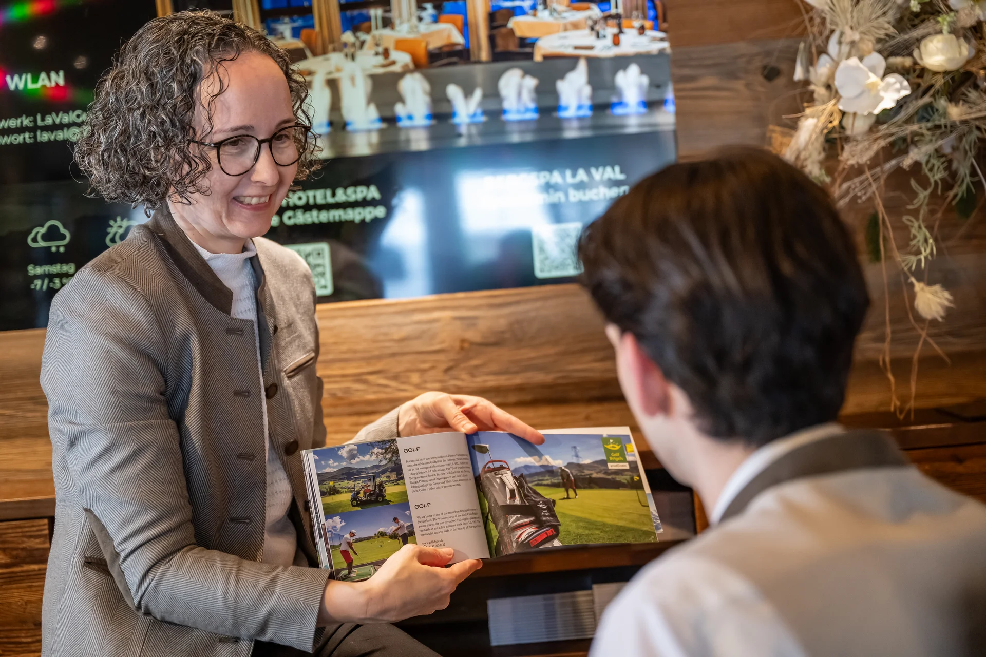 Frau zeigt einem Mann Prospekt mit Bildern von Golfplatz und Aktivitäten