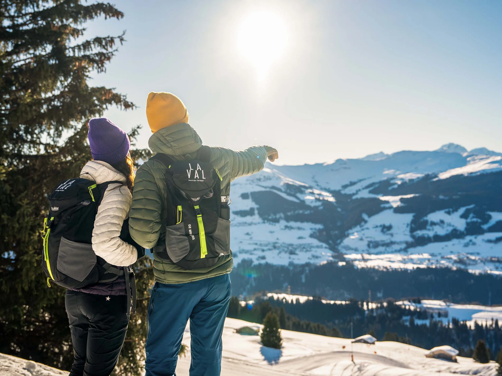Zwei Wanderer mit Rucksäcken blicken auf verschneite Alpen im Sonnenschein