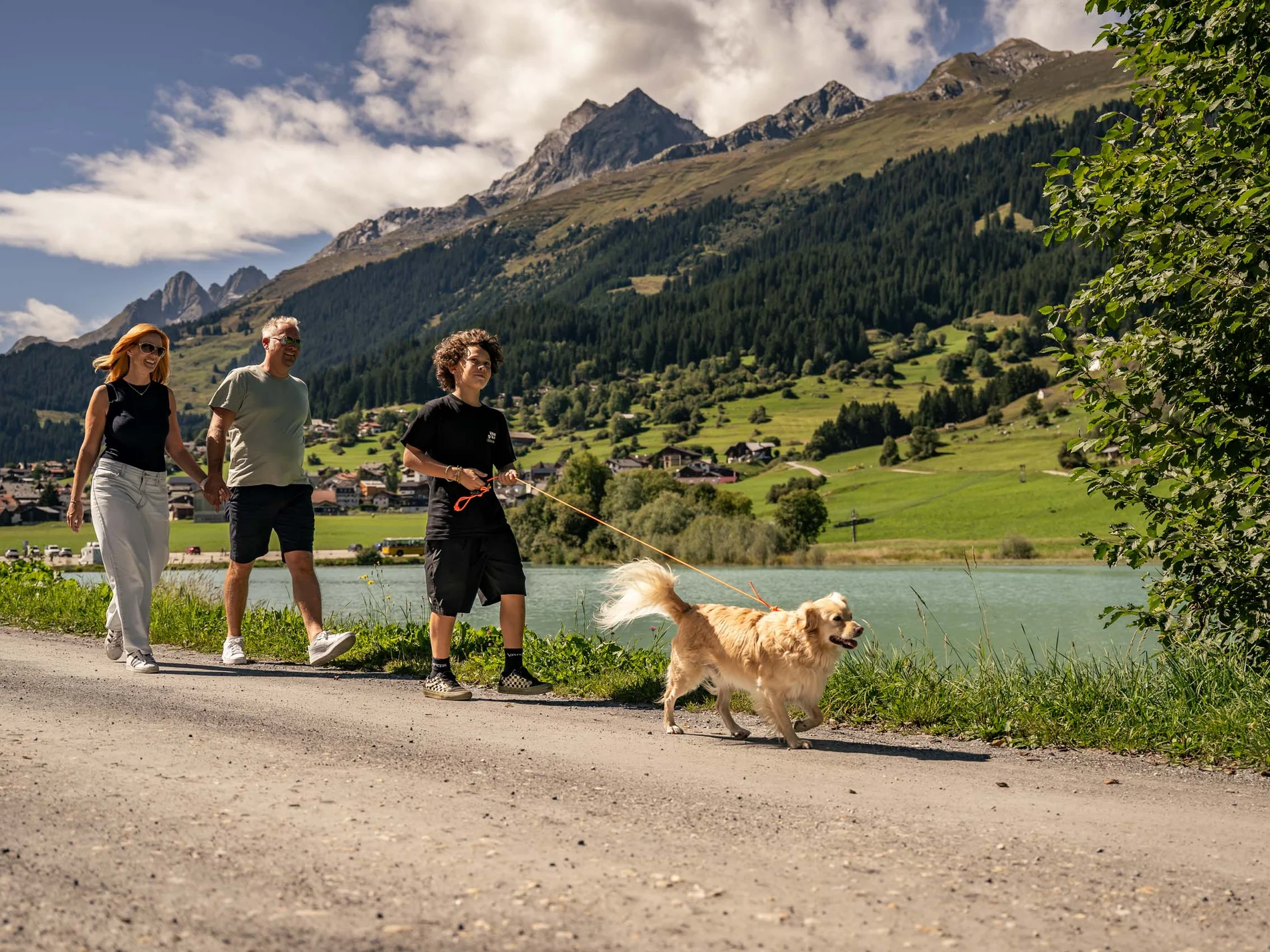 Familie spaziert mit Hund auf Weg neben See in den Bergen