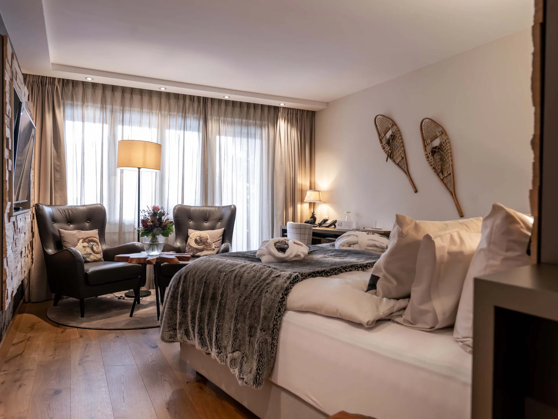 Gemütliches Hotelzimmer mit Doppelbett, zwei Sesseln und Dekoration an der Wand