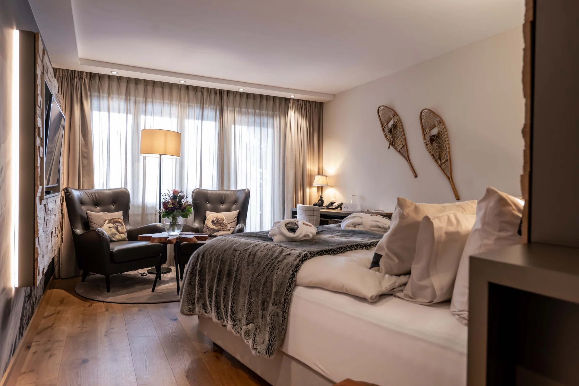 Gemütliches Hotelzimmer mit Doppelbett, zwei Sesseln und Dekoration an der Wand