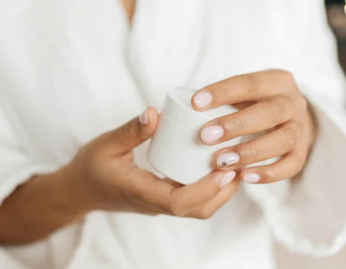 Person hält eine weiße Kosmetik- oder Pflegecreme im Bademantel