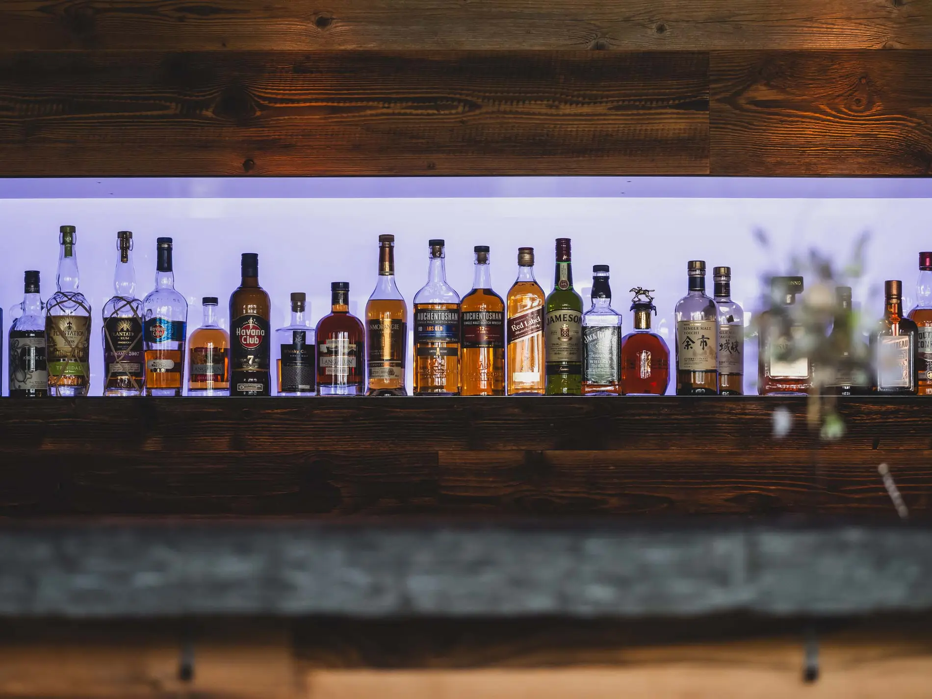Kulinarische Vielfalt in unseren Restaurants in Brigels Verschiedene Spirituosenflaschen auf einem beleuchteten Holzregal