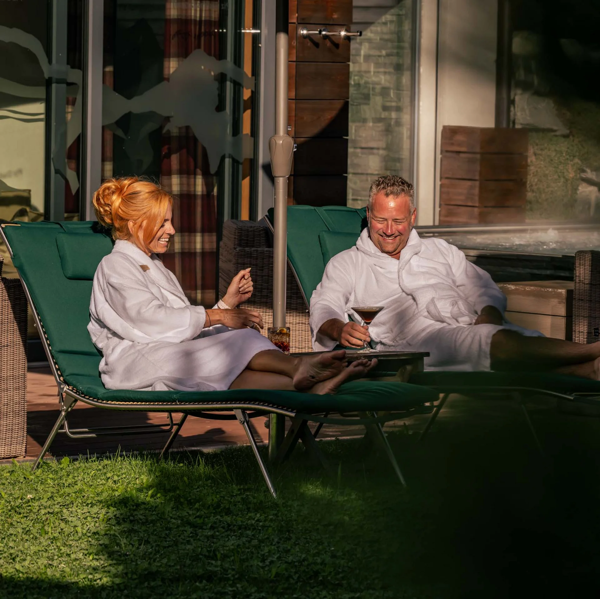 Paar entspannt im Bademantel auf Liegestühlen mit Getränken im Freien