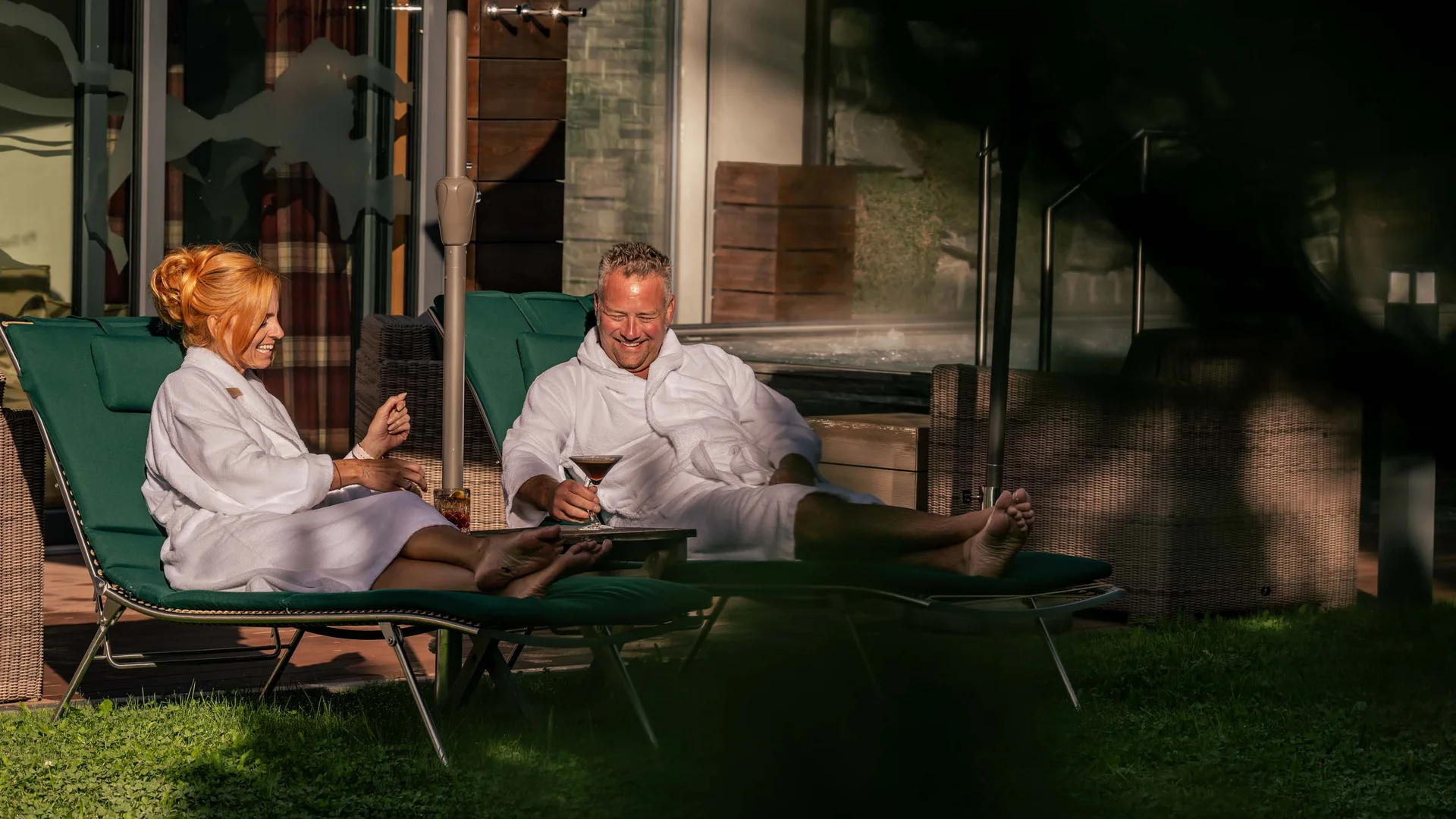 Paar entspannt im Bademantel auf Liegestühlen mit Getränken im Freien