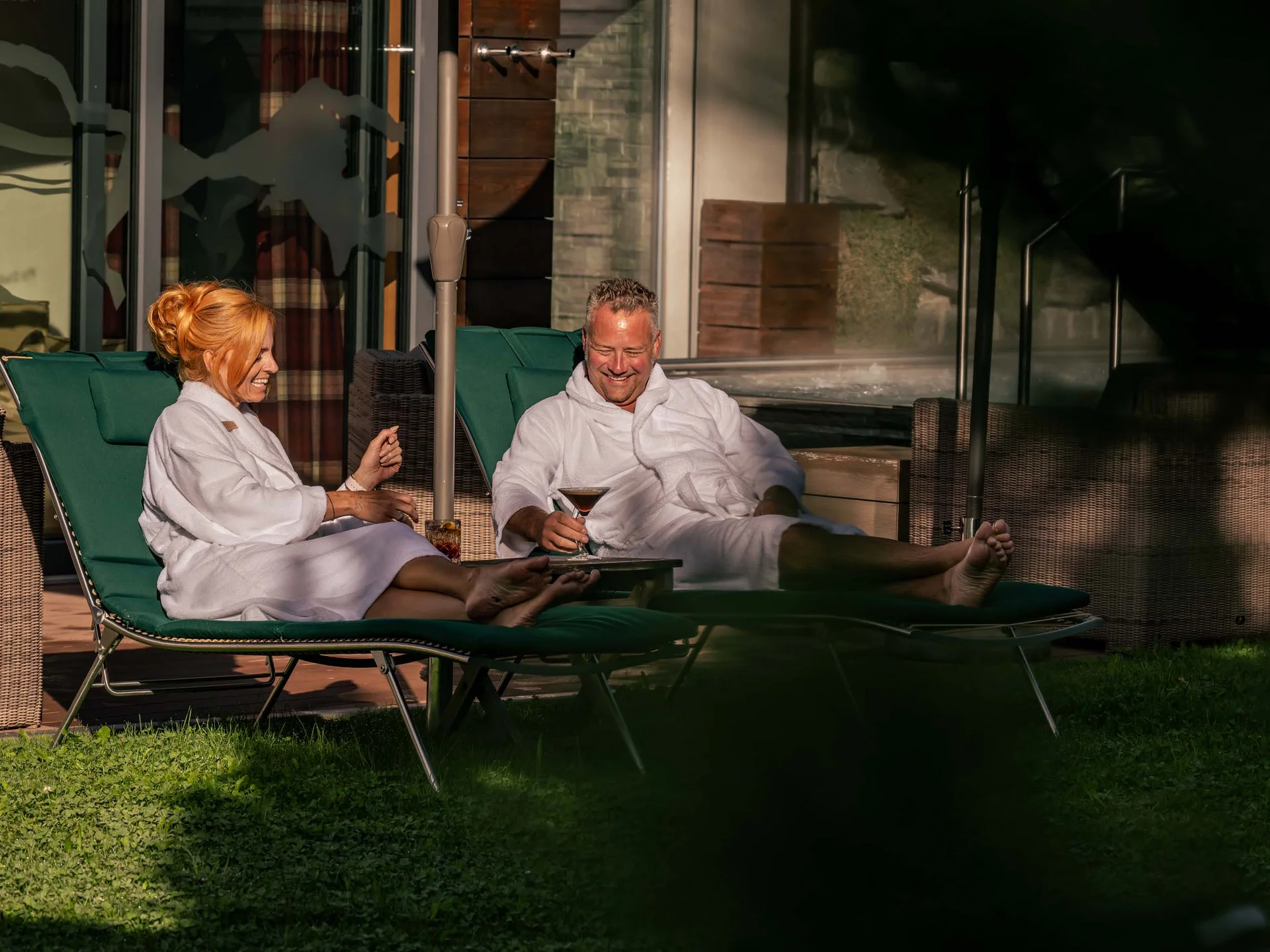 Paar entspannt im Bademantel auf Liegestühlen mit Getränken im Freien