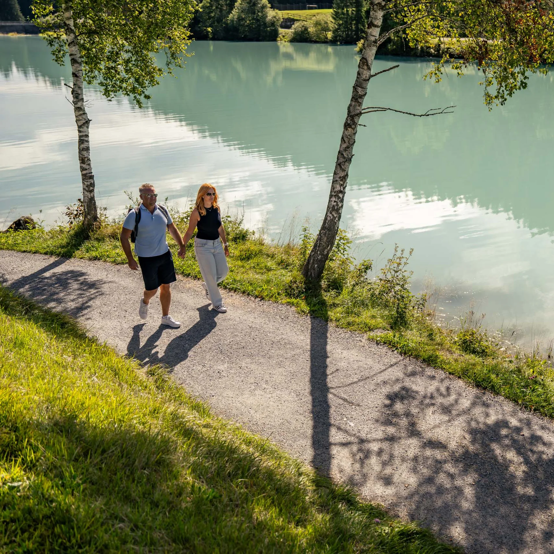 Paar spaziert an einem sonnigen Tag am Seeufer auf einem schattigen Weg