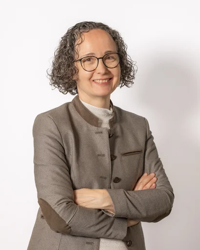 Frau mit kurzen lockigen Haaren und Brille lächelt mit verschränkten Armen