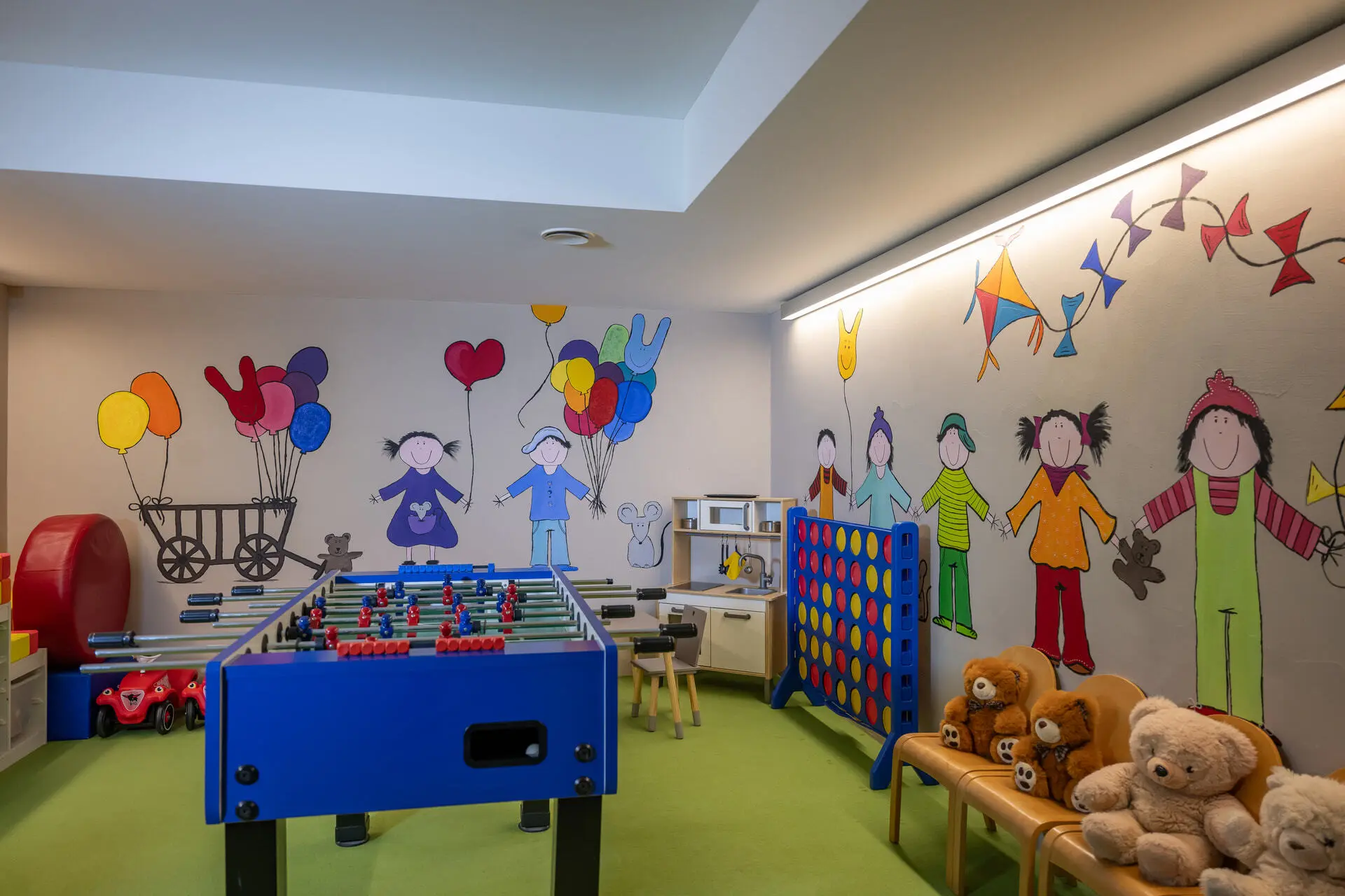 Eindrücke aus dem La Val Hotel & Spa Kinderspielzimmer mit Tischfußball, Wandmalerei und Kuscheltieren auf Stühlen