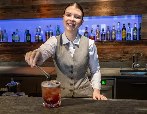 Lächelnde Barkeeperin serviert einen Cocktail an der Bar
