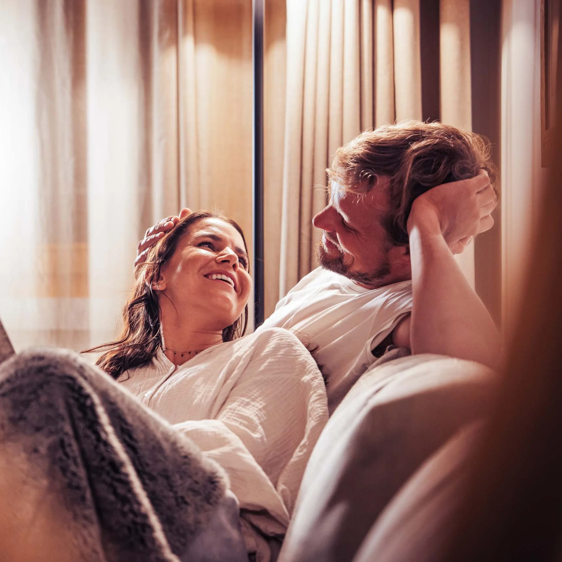 Paar kuschelt auf der Couch unter Decke, Frau hält Buch in der Hand